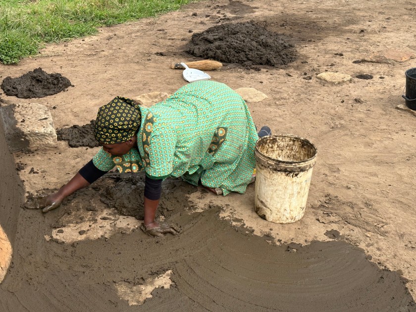 Basotho Cultural Village: vrouw in groen kleed wrijft mest open op grond. 