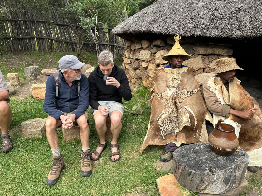 Basotho Cultural Village: twee toeristen drinken Umqombothi naast twee traditioneel-geklede Basotho-krijgers. 