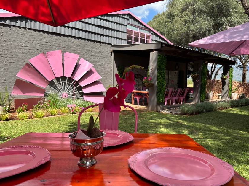 Die Boervouw Deli: roze tafel met roos bestek in tuin.