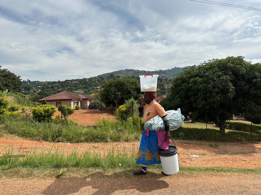 Afrikaanse vrouw met plastic emmer op hoofd.