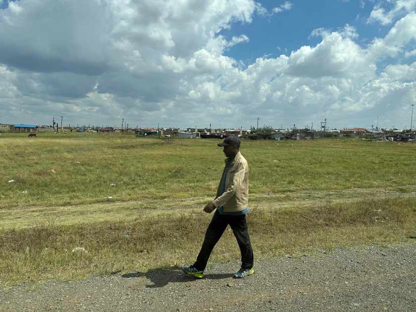 Sasolburg: eenzame man voor grasveld met armoedige wijk op achtergrond. 