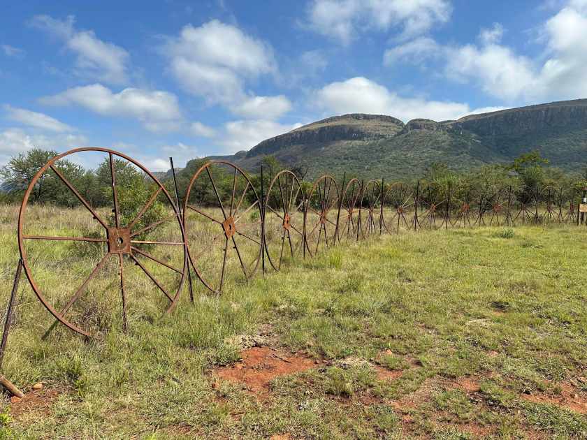 Vergenoeg, Magaliesberg: roestige ijzeren wielen op een rij in Afrikaans berglandschap.