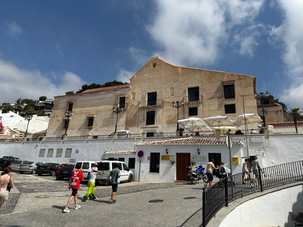 Beige gebouw op helling met witte muren een verdieping lager. 