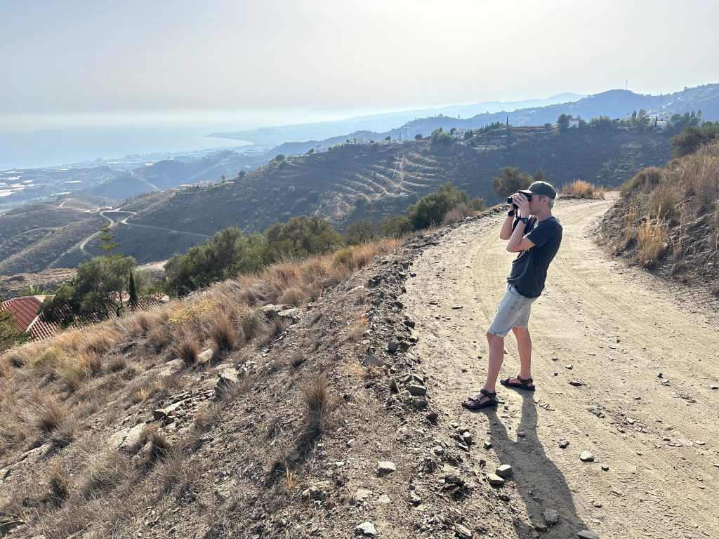 Toerist op grindpad kijkt met verrekijker naar panorama. 