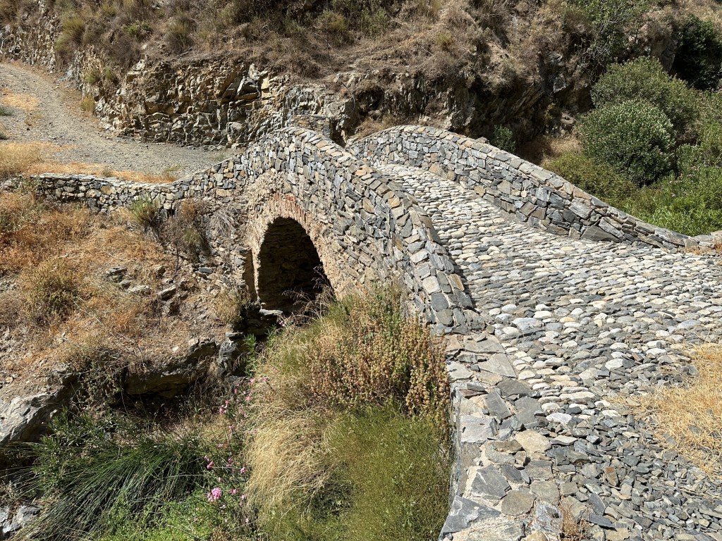 Boogbrug van Sedella met groen begroeide helling links.
