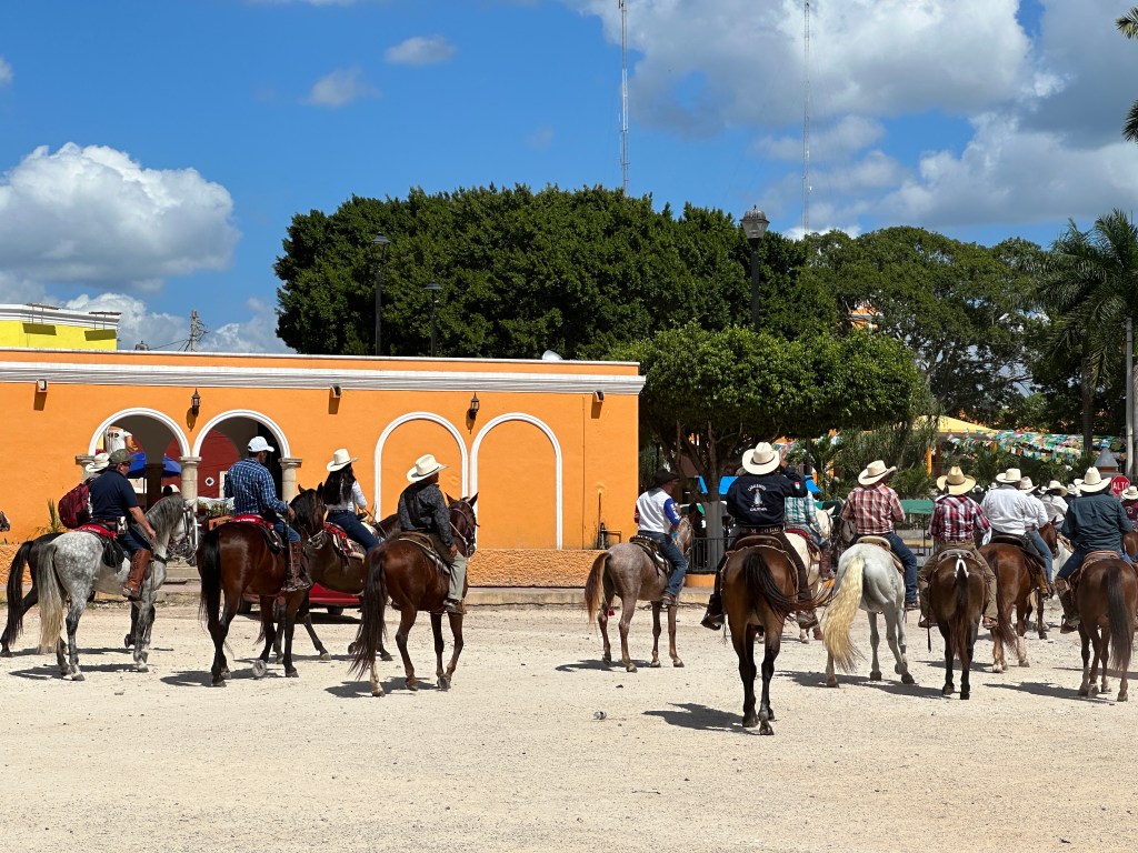 Cabalgata: ruiters voor okergeel gebouw. 
