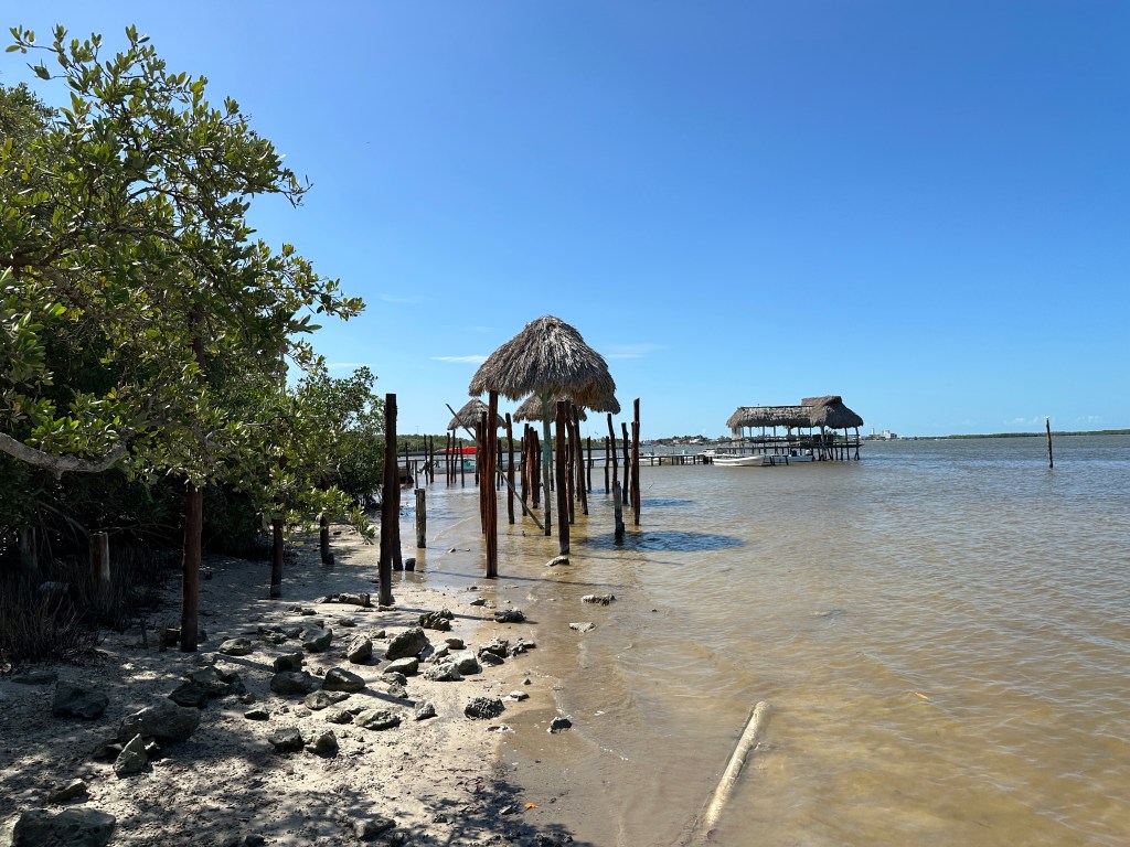 Palen met strooien dakjes op door vloed overspoeld strand. 