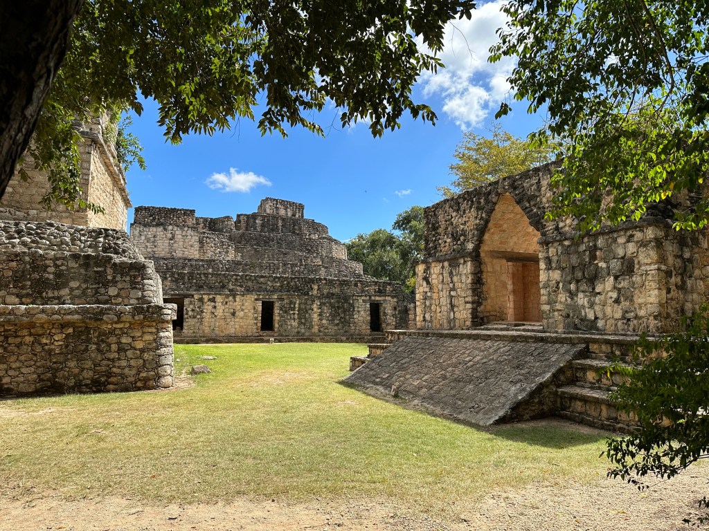 Ruïnes met driehoeksgewelf rond grasveld. 