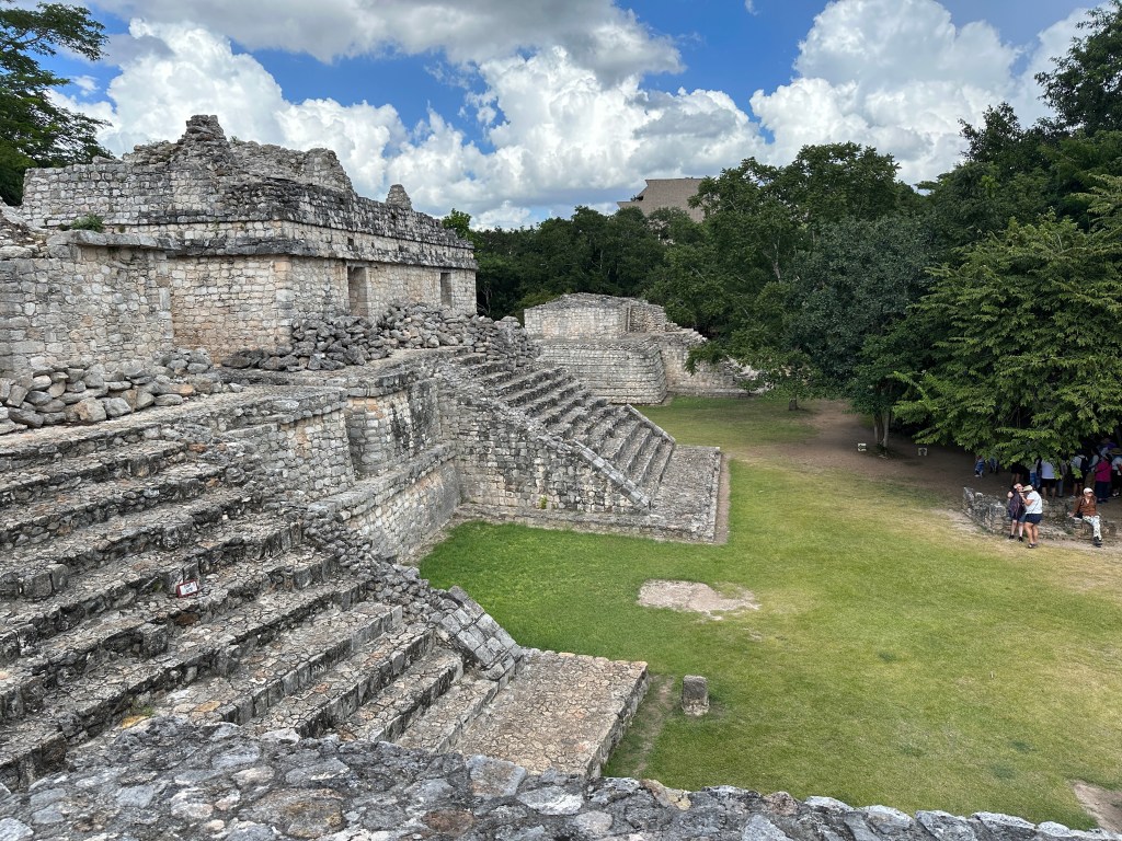 Ruïnes van gebouwen met trappen links en bos, rechts. 