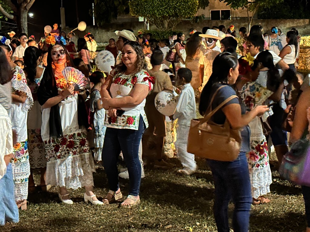 Tientallen Mexicanen in traditionele klederdracht en beschilderde gezichten verzamelen voor het avondfeest. 