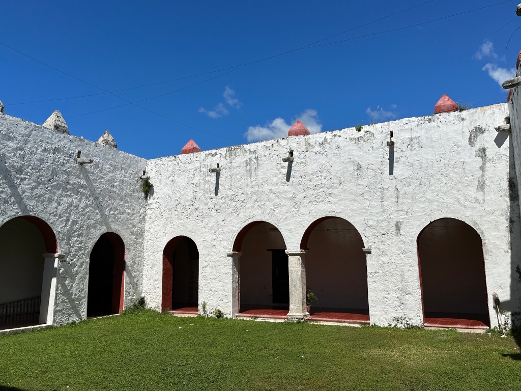 Binneplein van klooste: witte muren met bogen en grasveld. 