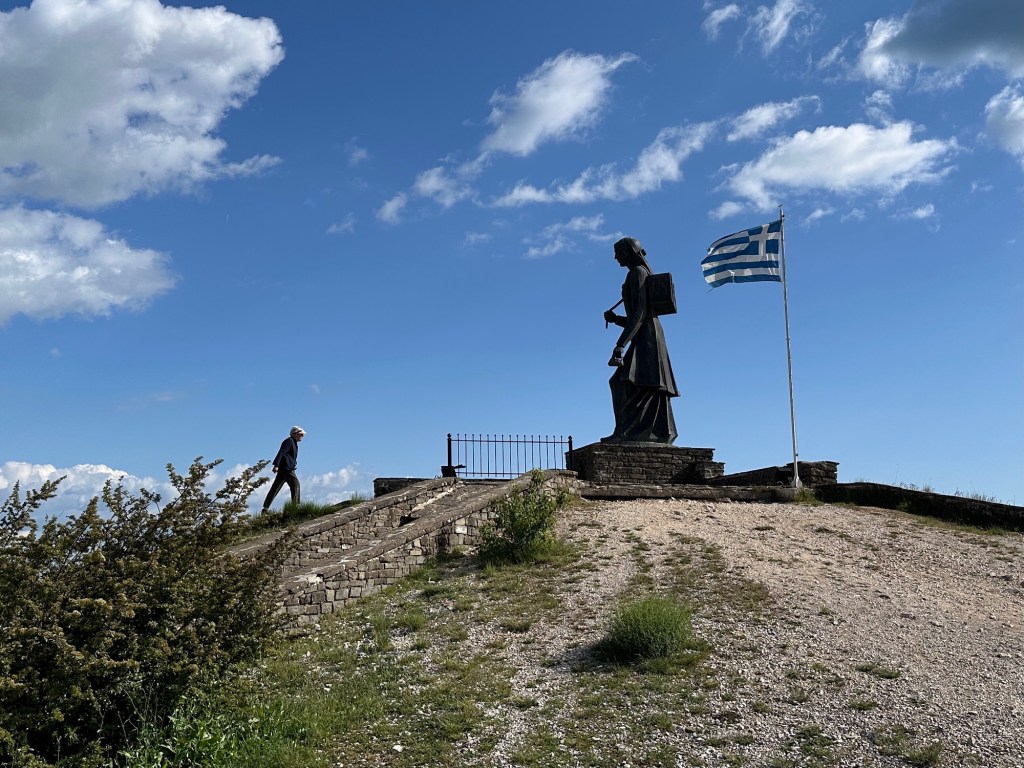 Monument vrouw van Zagori (groot standbeeld, Griekse vlag, blauwe lucht) in Zagori, Centraal Griekenland