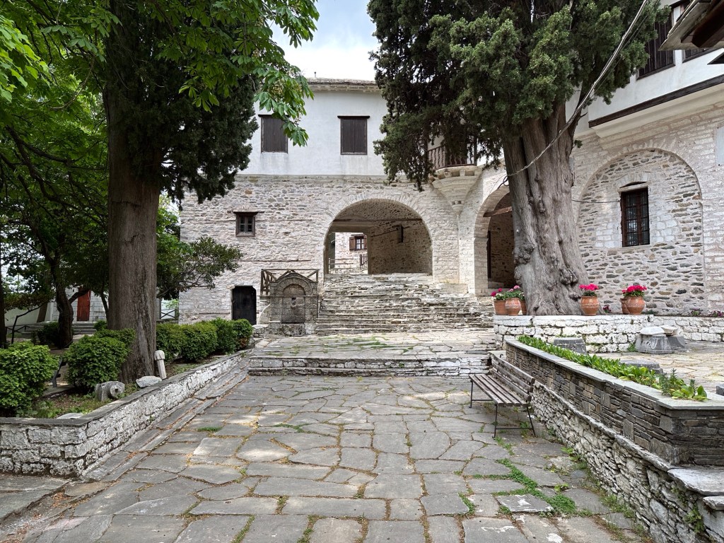 Grijze stenen gebouwen rond binnenplein met bomen in Makrinitsa, Pelion
