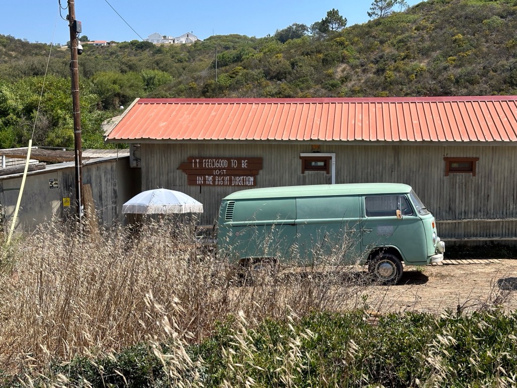 Blauwgroen VW minibus voor huis met tekst “It feels good to be lost in the right direction” aan Praia do Carvalhal