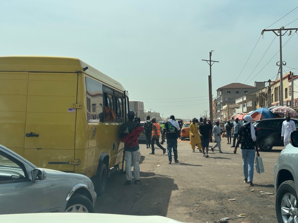 Auto’s, veel mensen die in een geel busje stappen