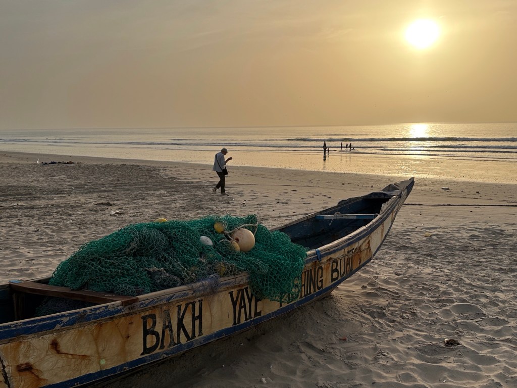 Oude pirogue op het strand, enkele mensen, zonsondergang 
