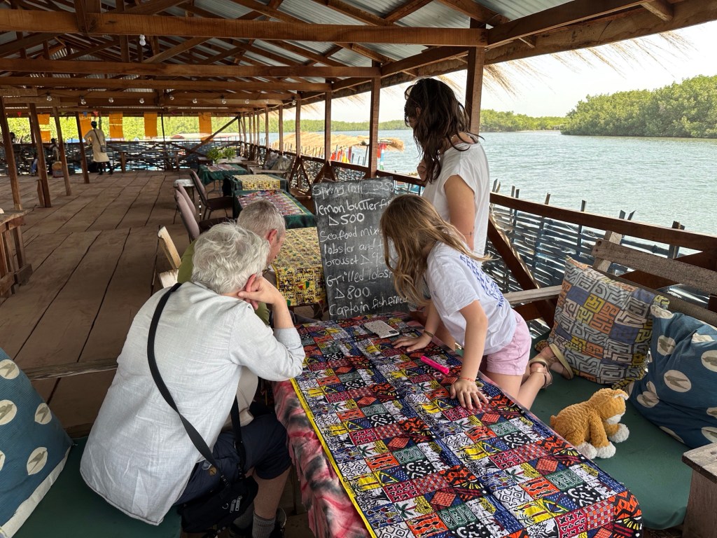 Toeristen bekijken op bord geschreven menu in hangar van DOdou’s restaurant