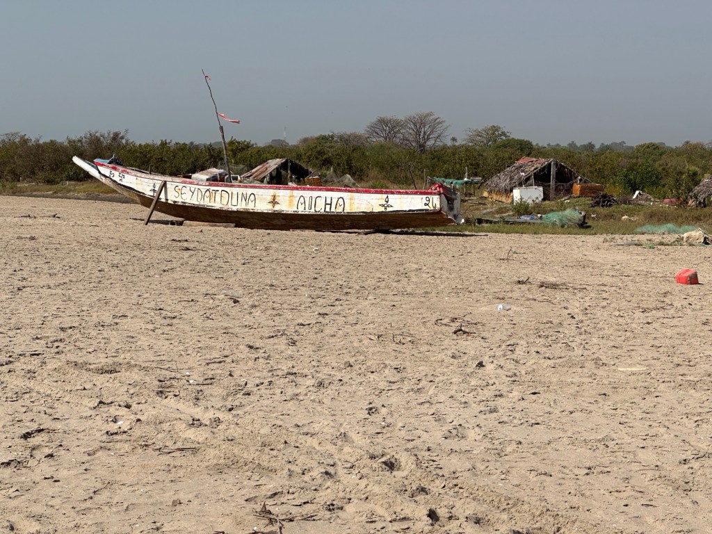 Oude, witte pirogue naast klein traditioneel hutje op strand