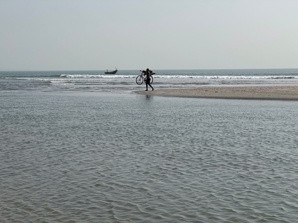 Fietser met fiets op schouder verlaat zandbank in zee