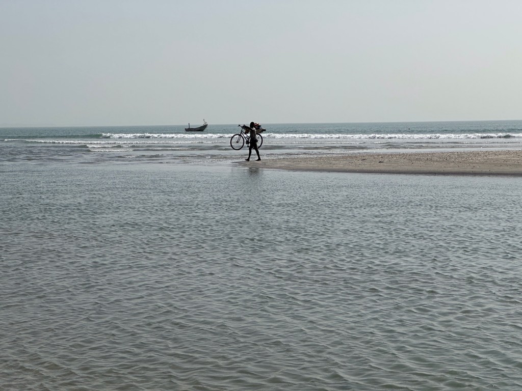 Fietser met fiets op schouder op zandbank in de zee