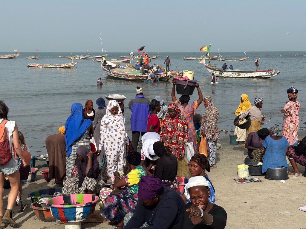 Mensen in veelkleurige kledij voor de zee met pirogues op achtergrond