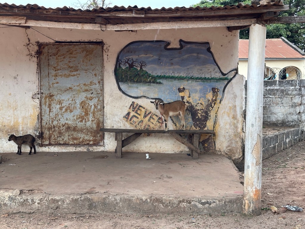 Muurschildering op oud huis: kaart van Afrika, Never Again tekst, echte geit staat op bank voor de muurschildering