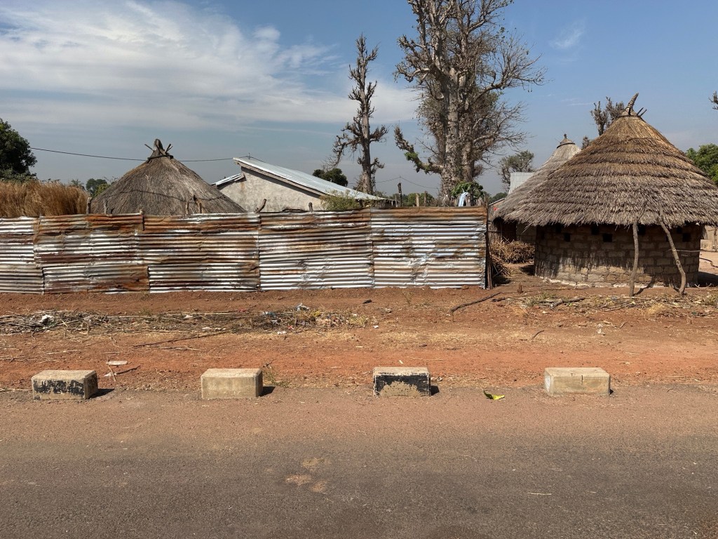 Straat met traditioneel Afrikaans huis met rieten dak en afsluiting van golfplaten