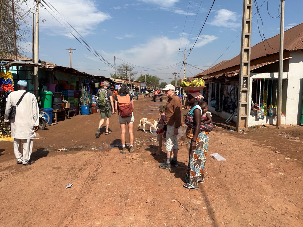 Straat, rode aarde, golfplaten winkeltjes in Basse