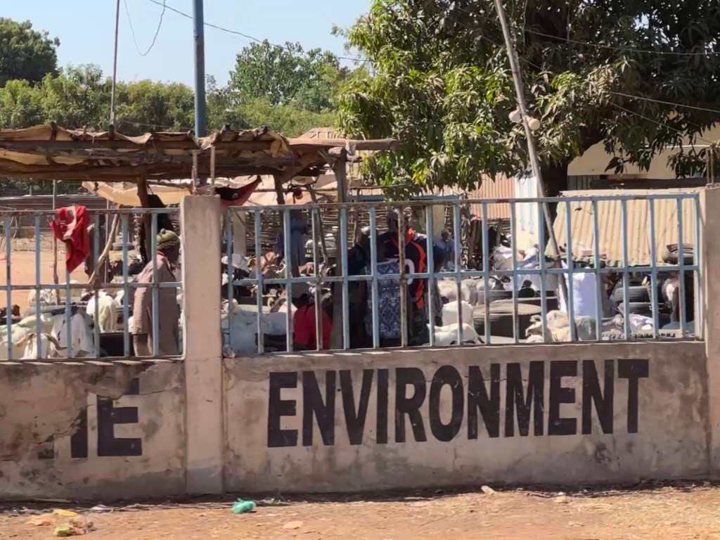 De veemarkt van Brikama met het woord “ENVIRONMENT” in grote zwarte letters op de muur