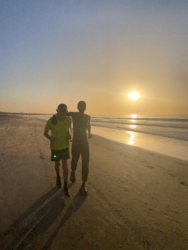 Jogger-toerist en lokale jogger bij zonsondergang op een strand in Gambia