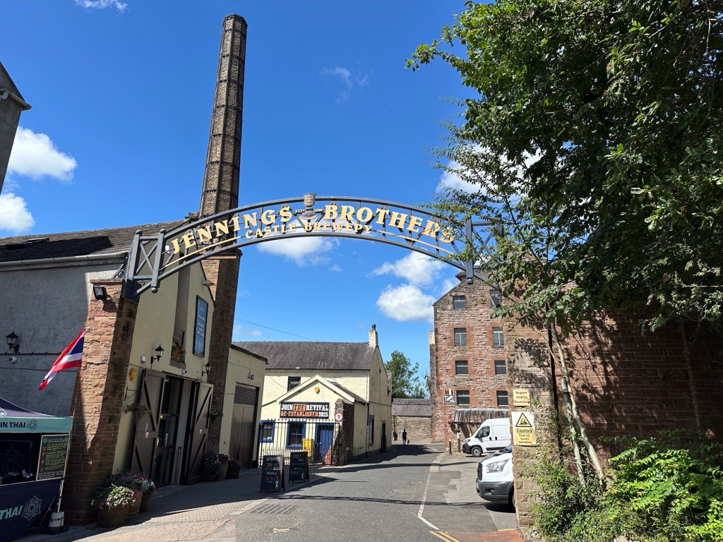 Metalen boog over straat met brouwerij-naam. 