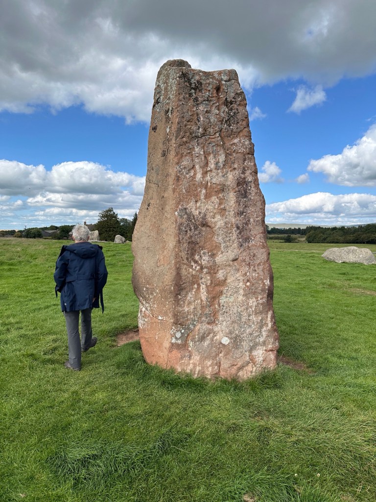 Grote, rode steen, 4 meter hoog met toeriste en groene weide. 
