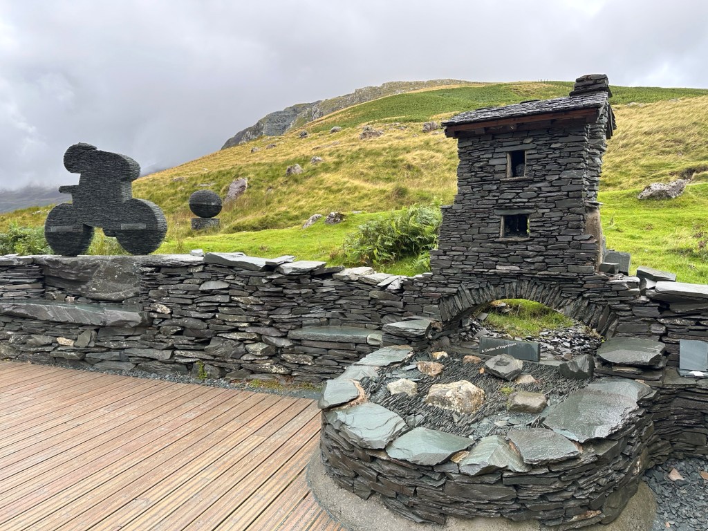 Gebeeldhouwd huisje en fietser in leisteen.