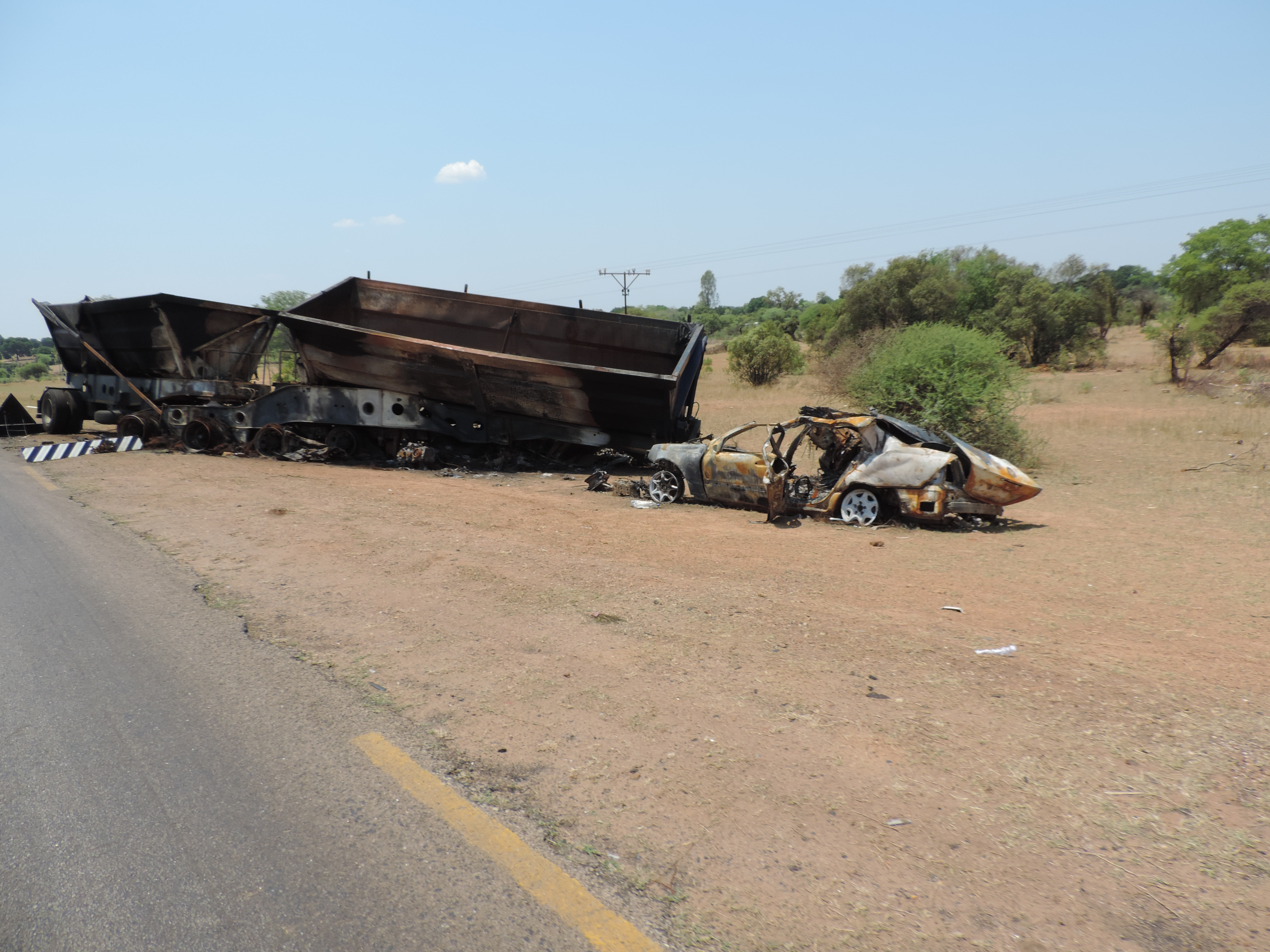 Wrak van truck naast asfaltweg in de savanne.