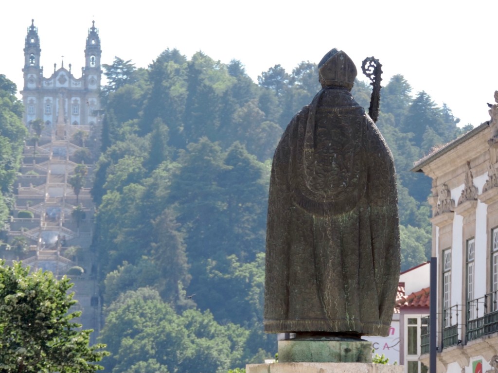Standbeeld van bisschop op de rug genomen met in de achtergrond de kerk. 
