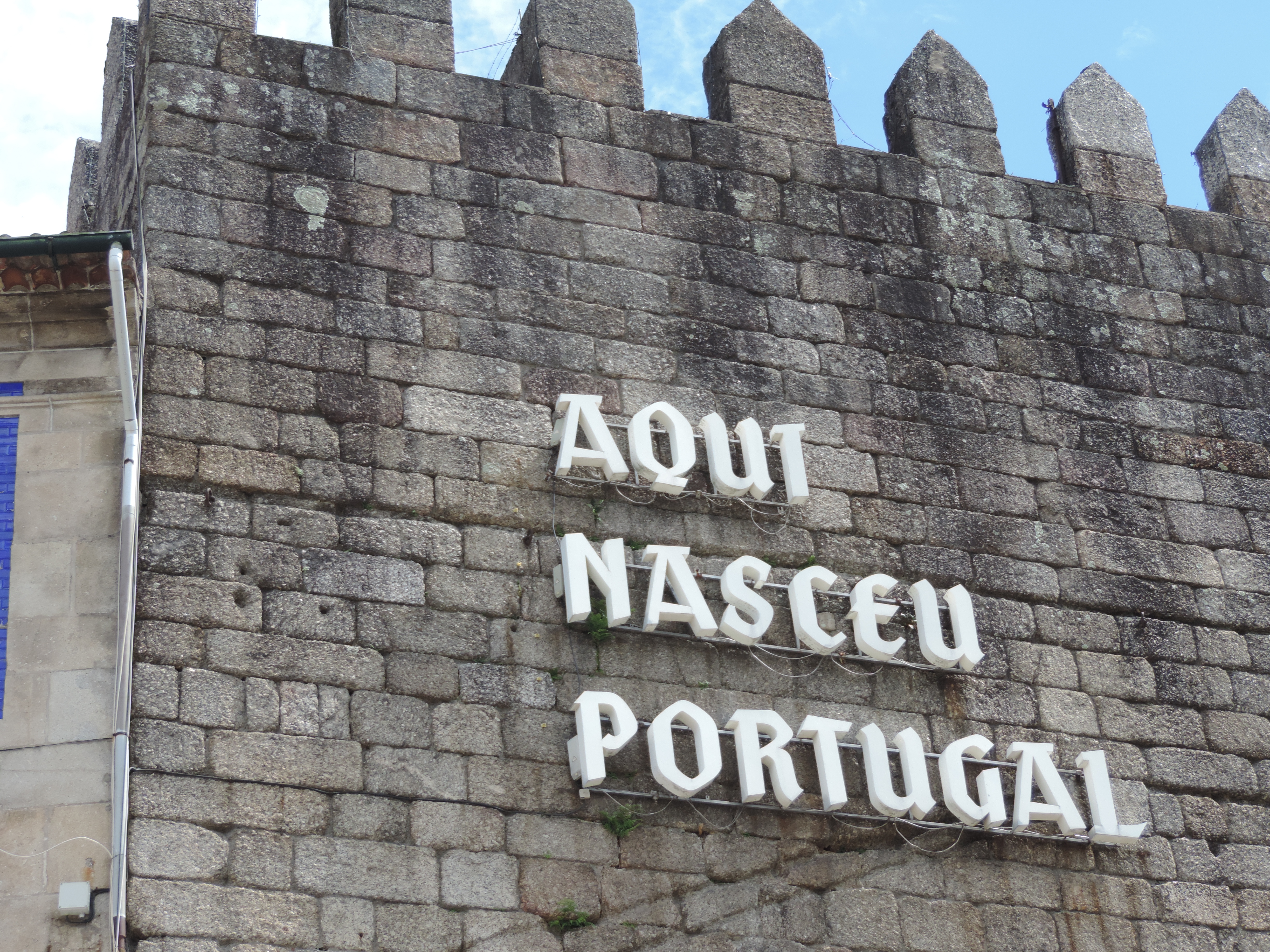 Grijze, oude stadsmuur met kantelen en opschrift in witte letters: Aqui Nasceu Portugal.