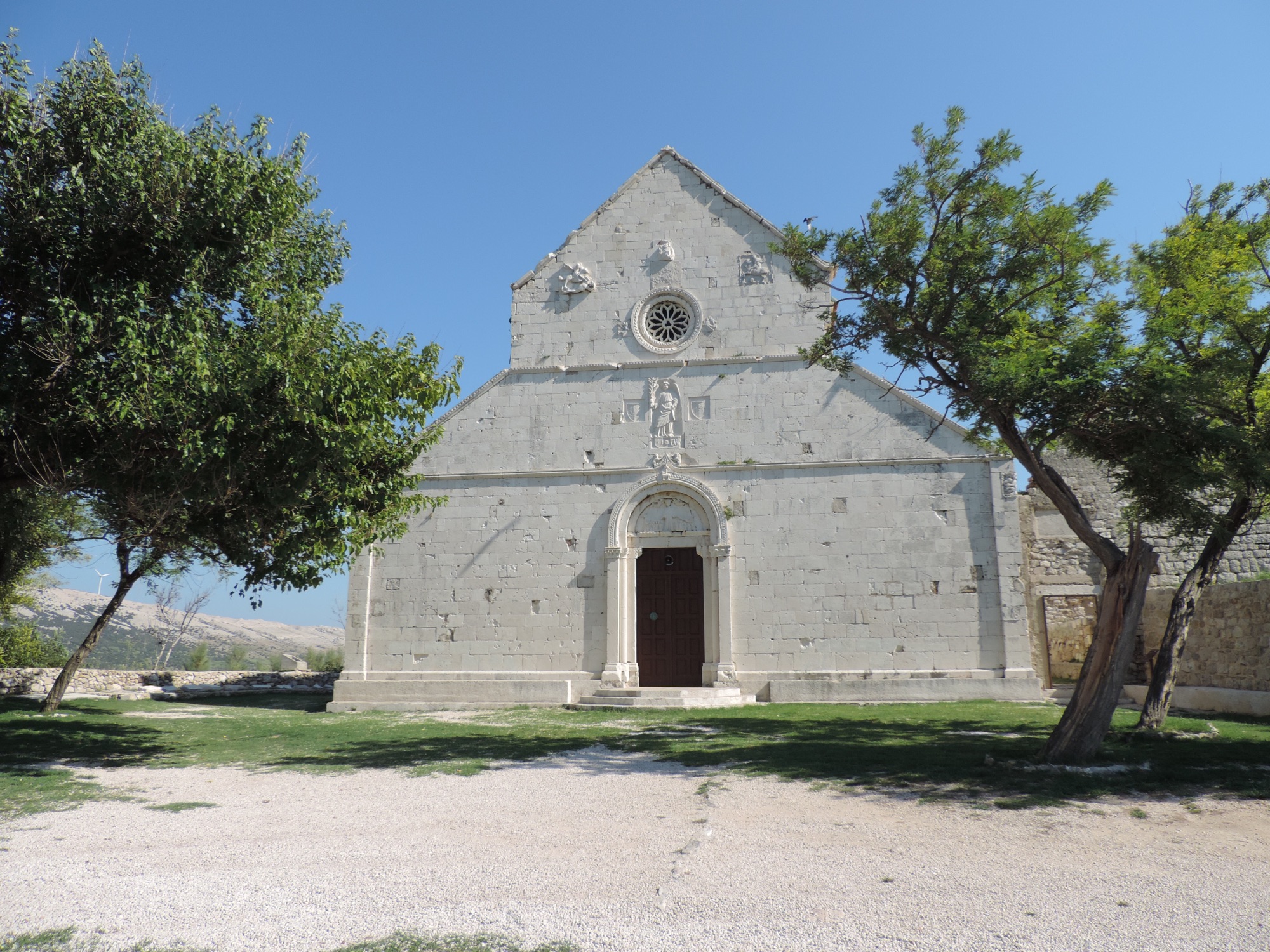 Wit kerkje tussen twee groene bomen.