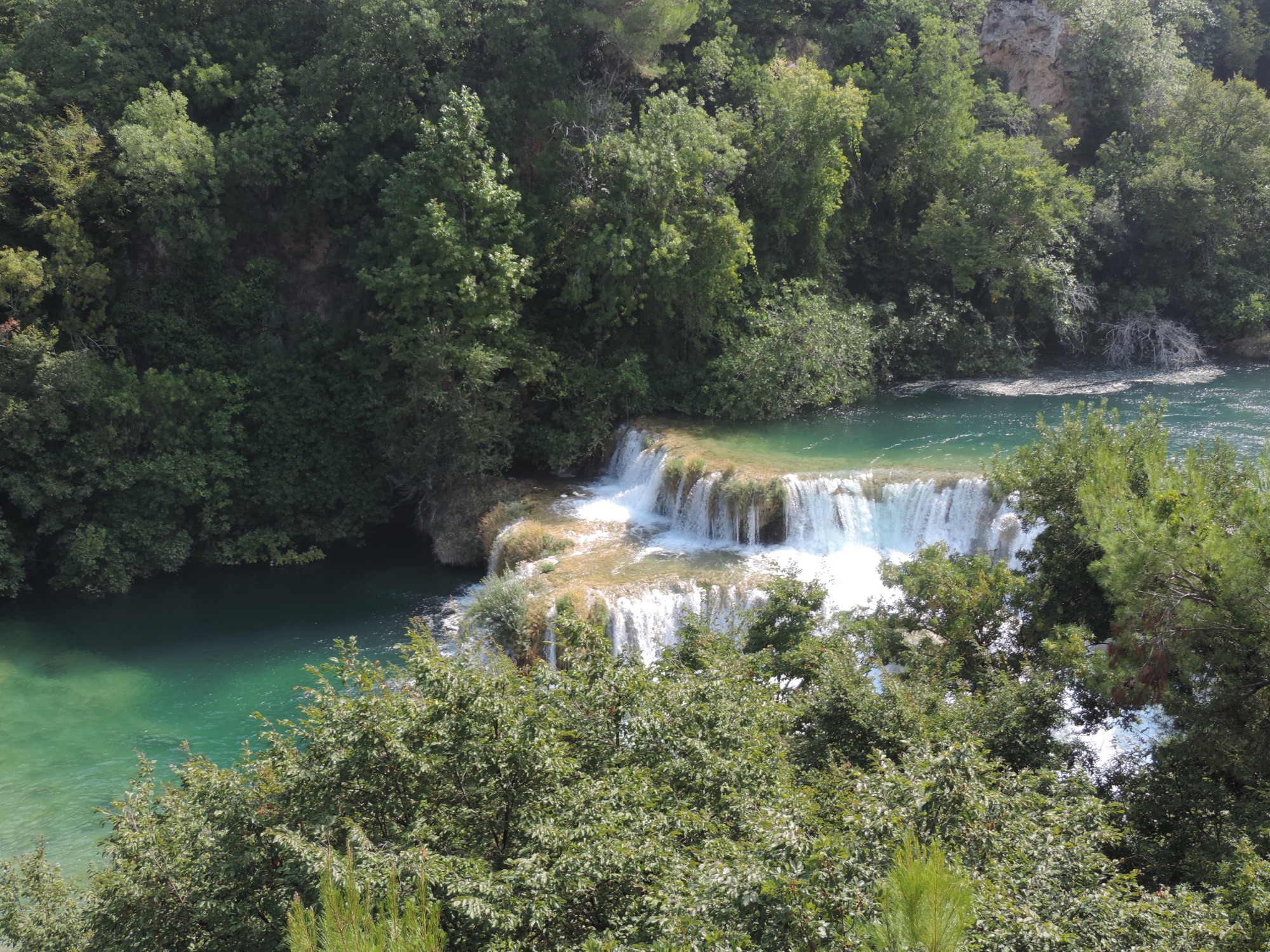 Waterval tussen bomen en blauwgroen water.