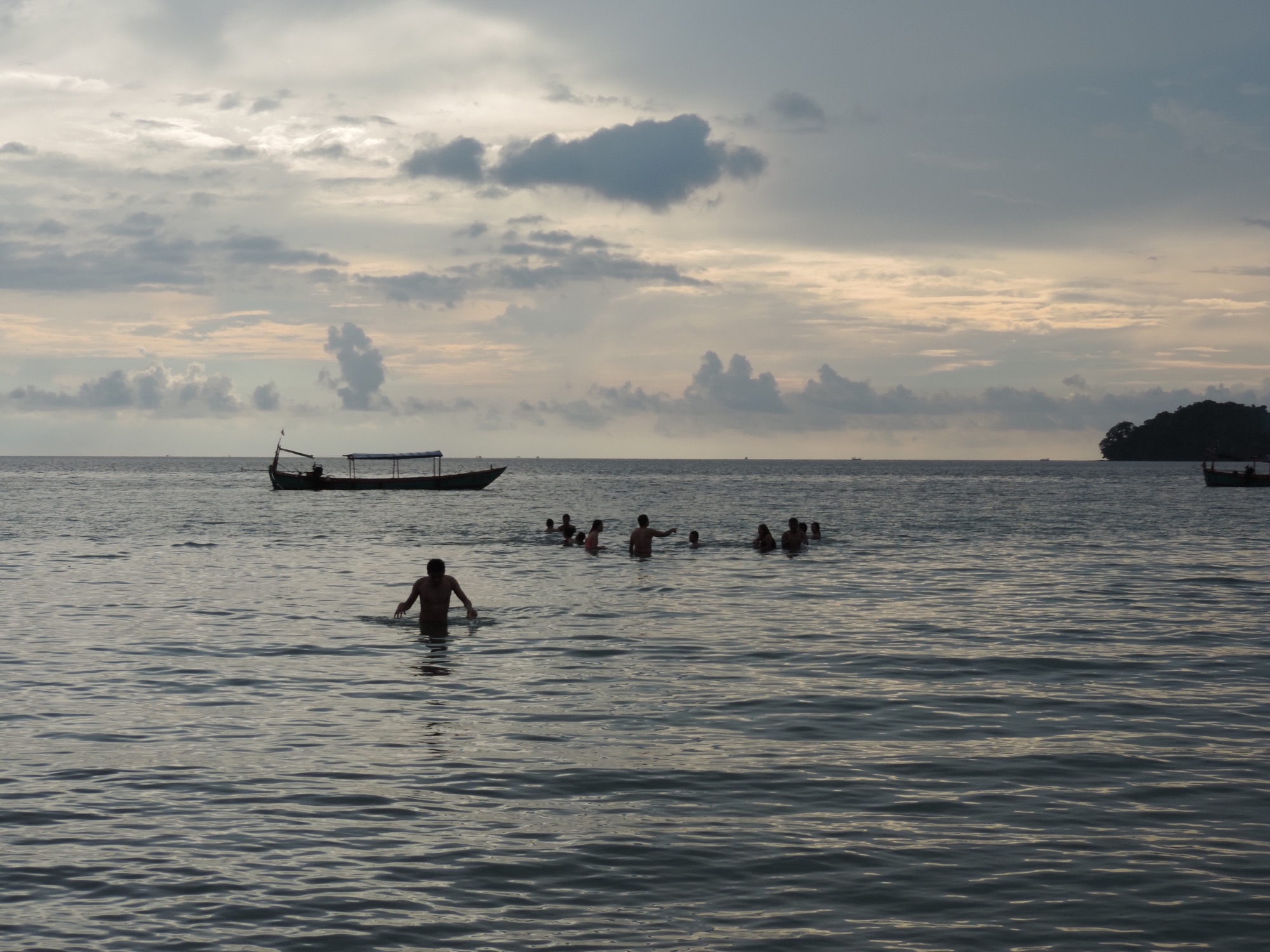 Zonsondergang met mensen in zee en sampan.