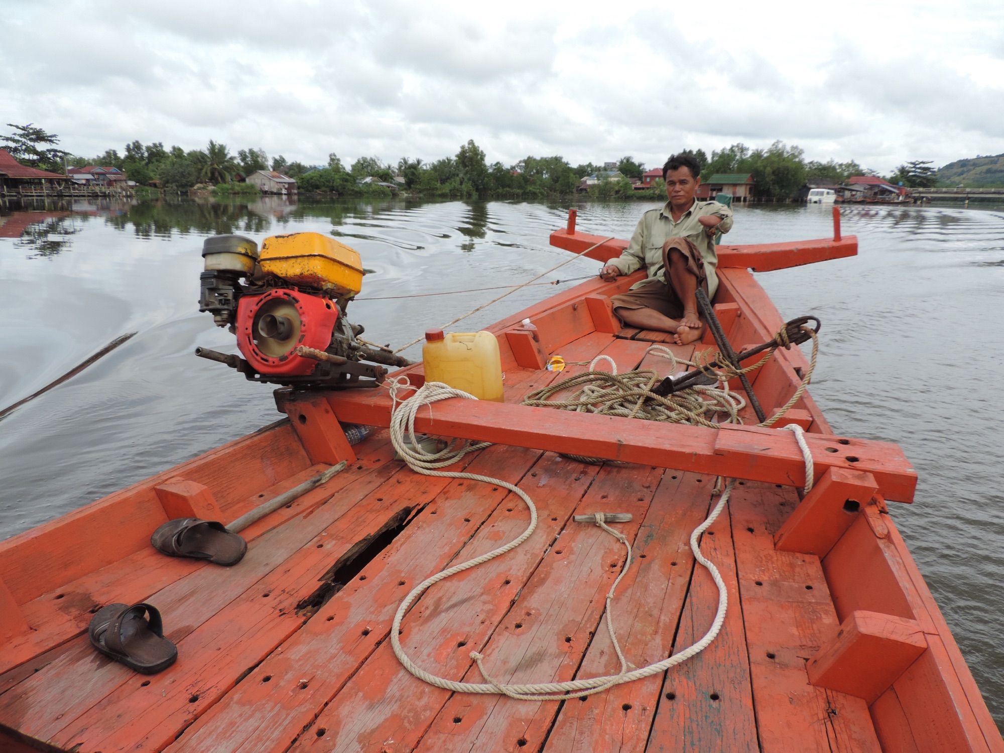 Eenarmige schipper op voorplecht van klein rood bootje 