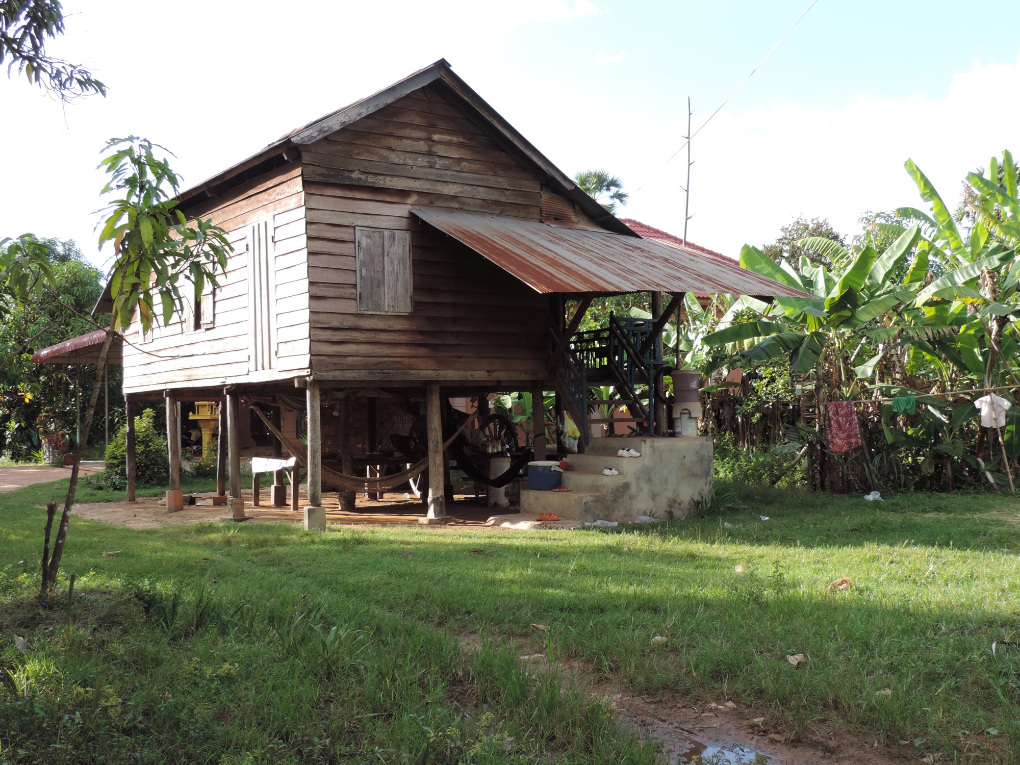 Houten huis op betonnen palen en palmbomen.