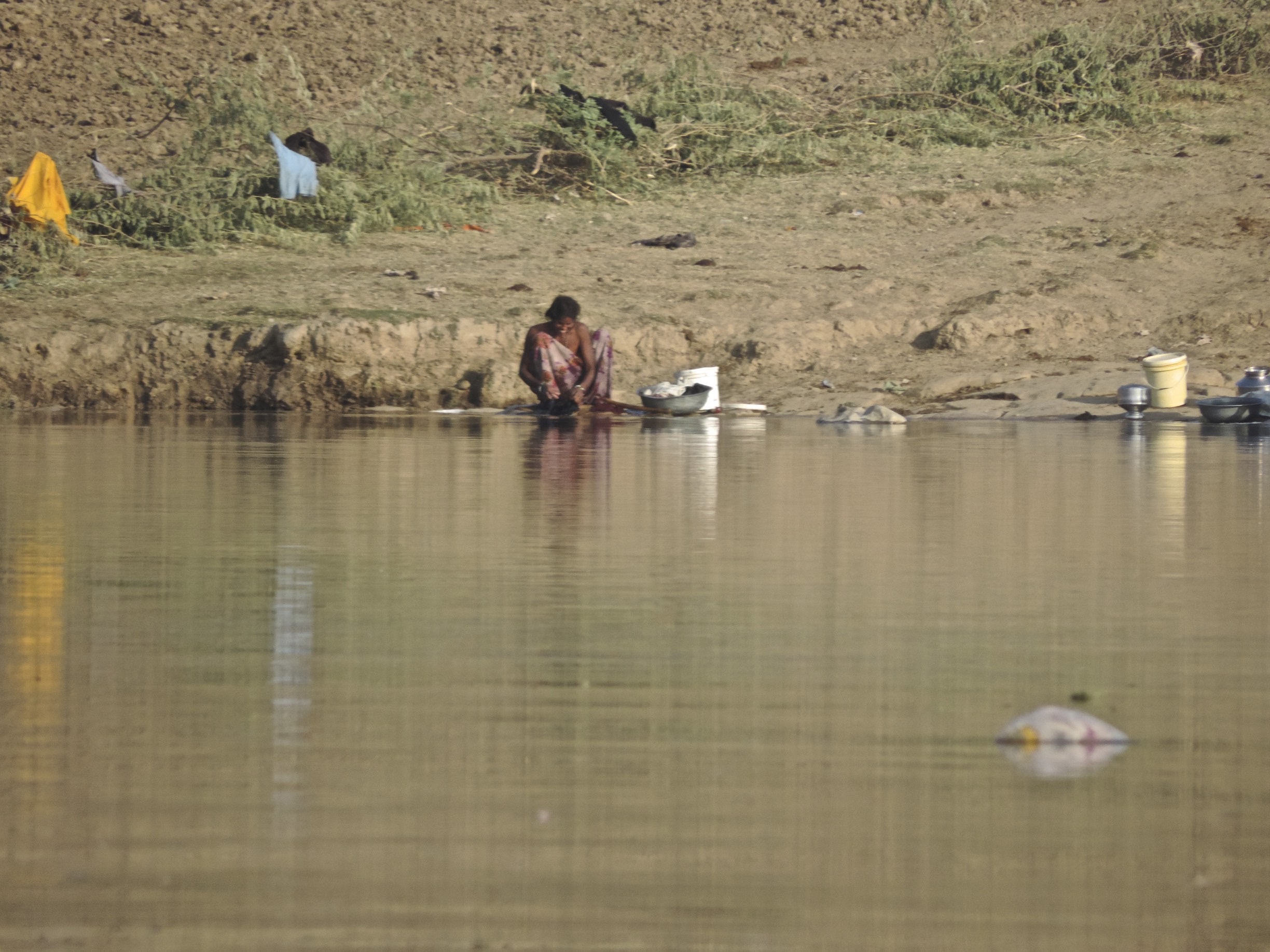 Vrouw wast kleding aan de rand van een rivier.