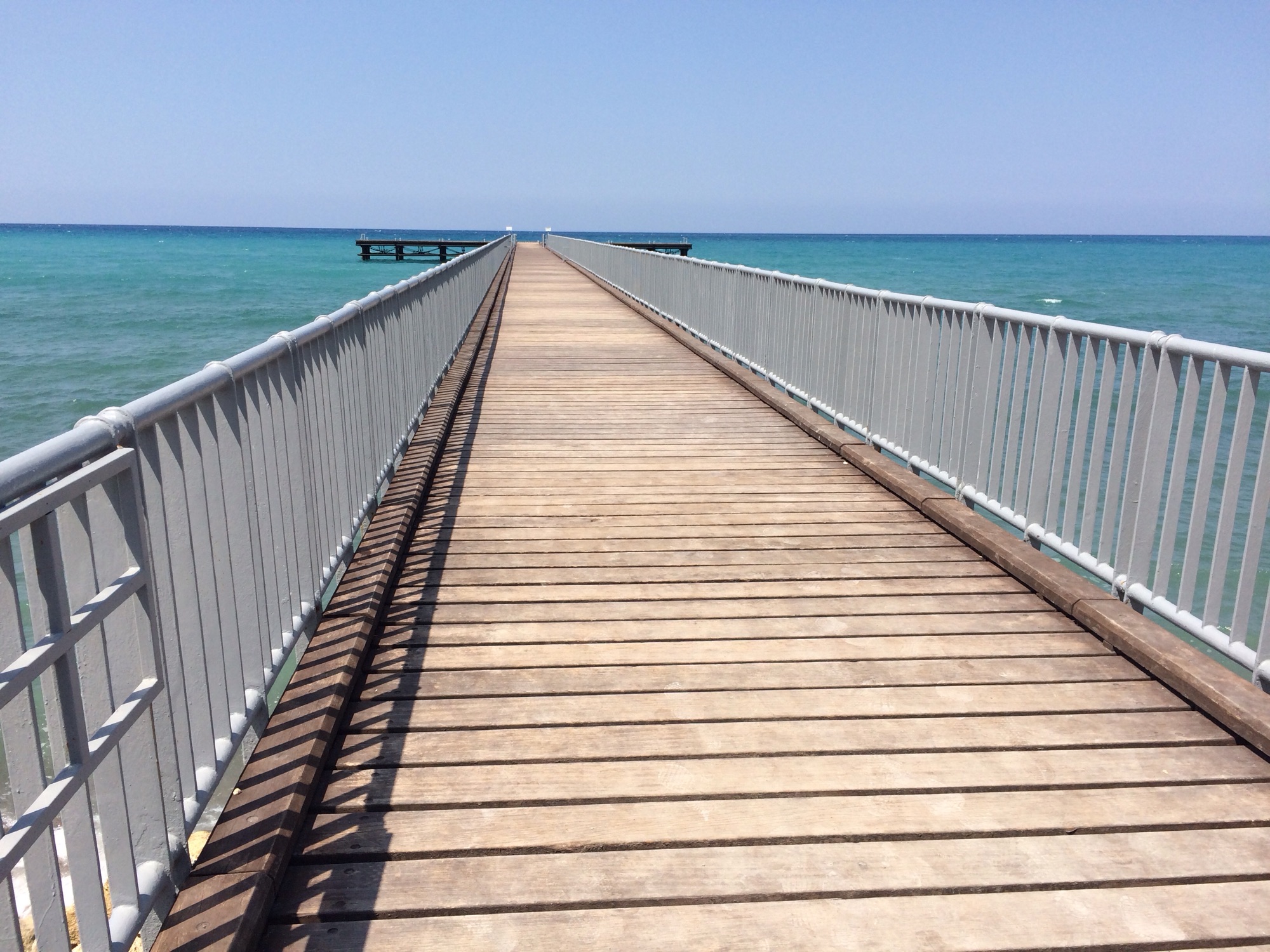 Eondeloos lijkende pier in blauwe zee.