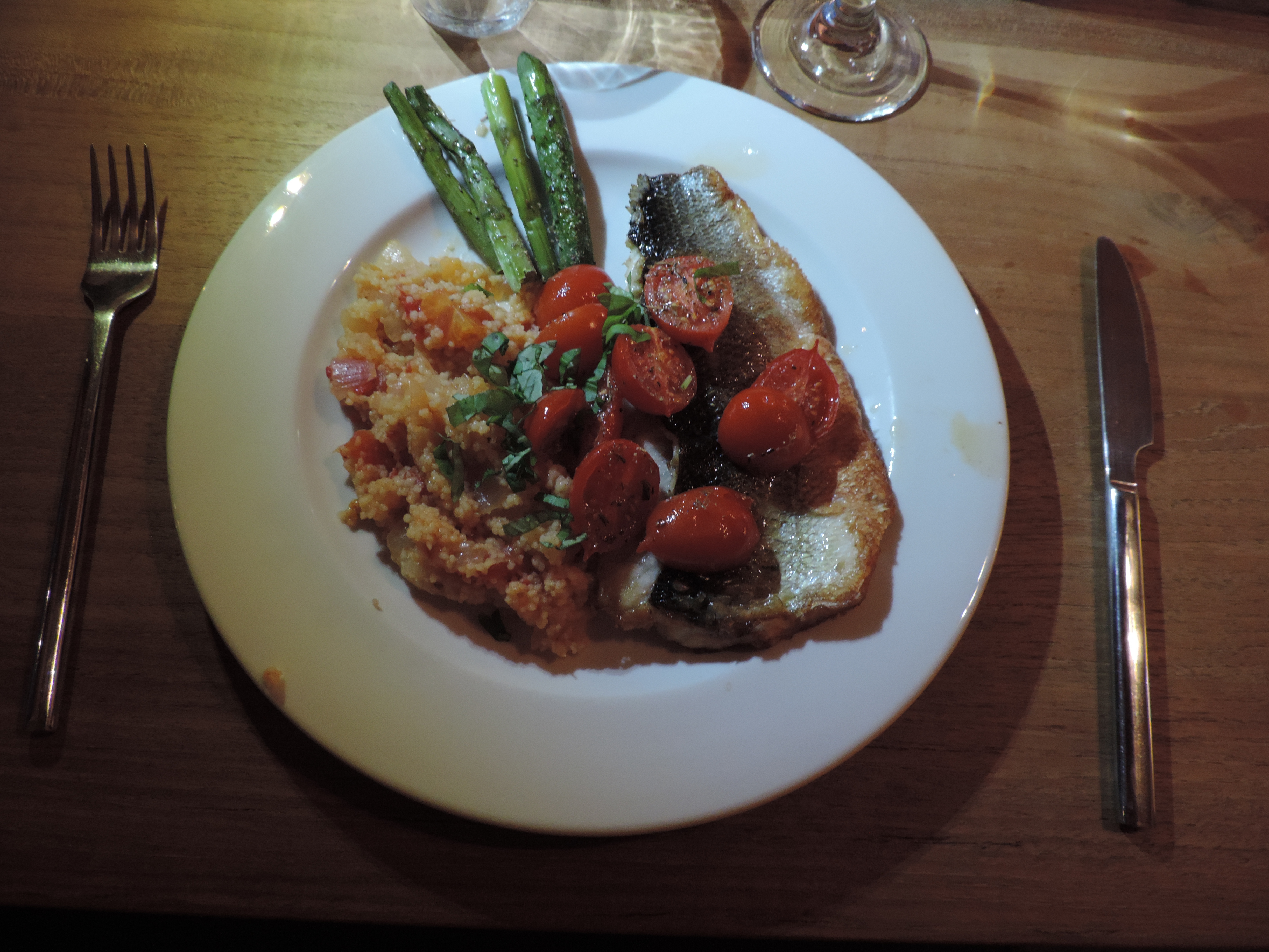 Bord met zeebaars, groene asperges, couscous en tomaatjes.