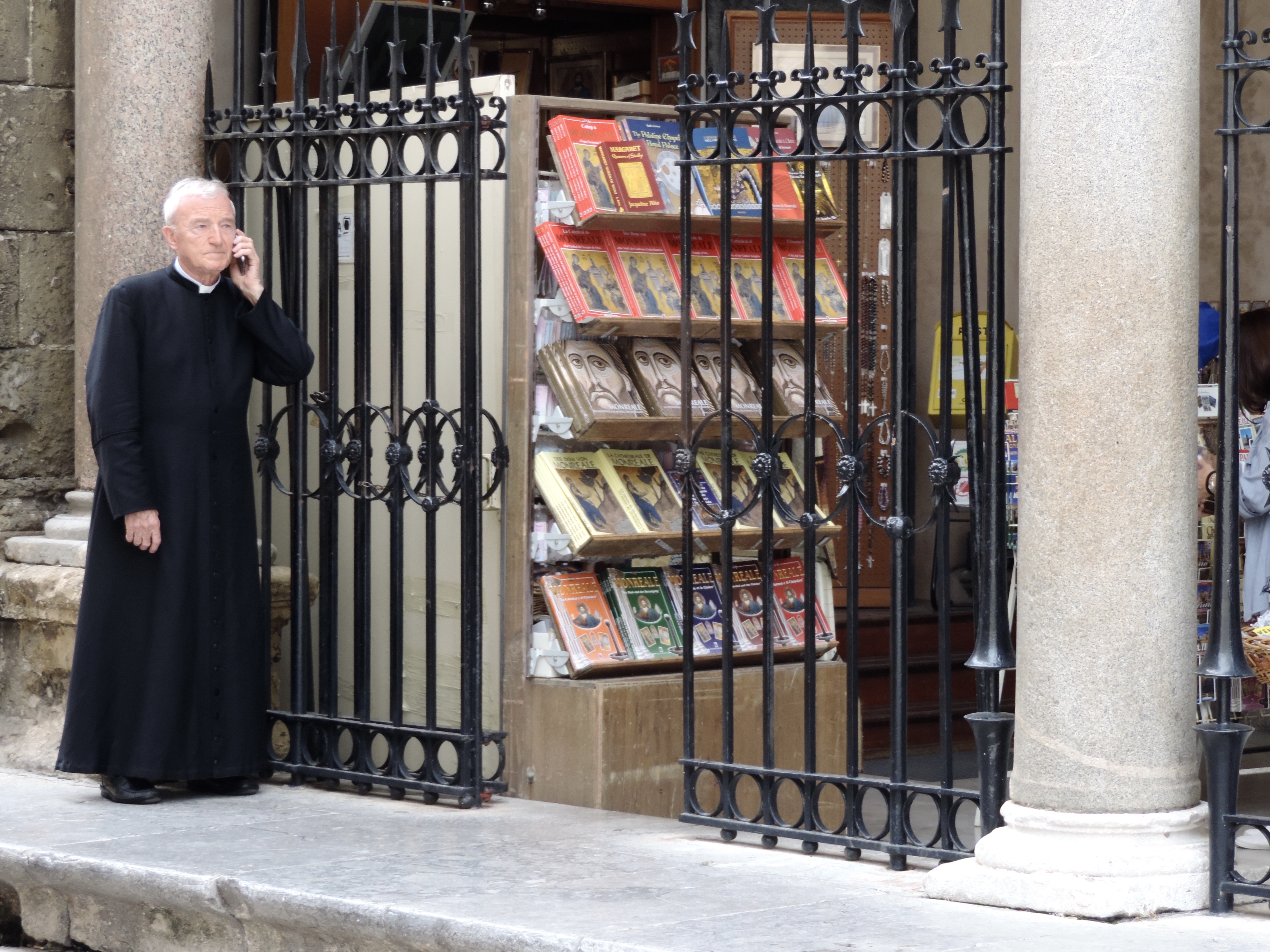 Telefonerende pastoor in habijt aan boekenwinkel.