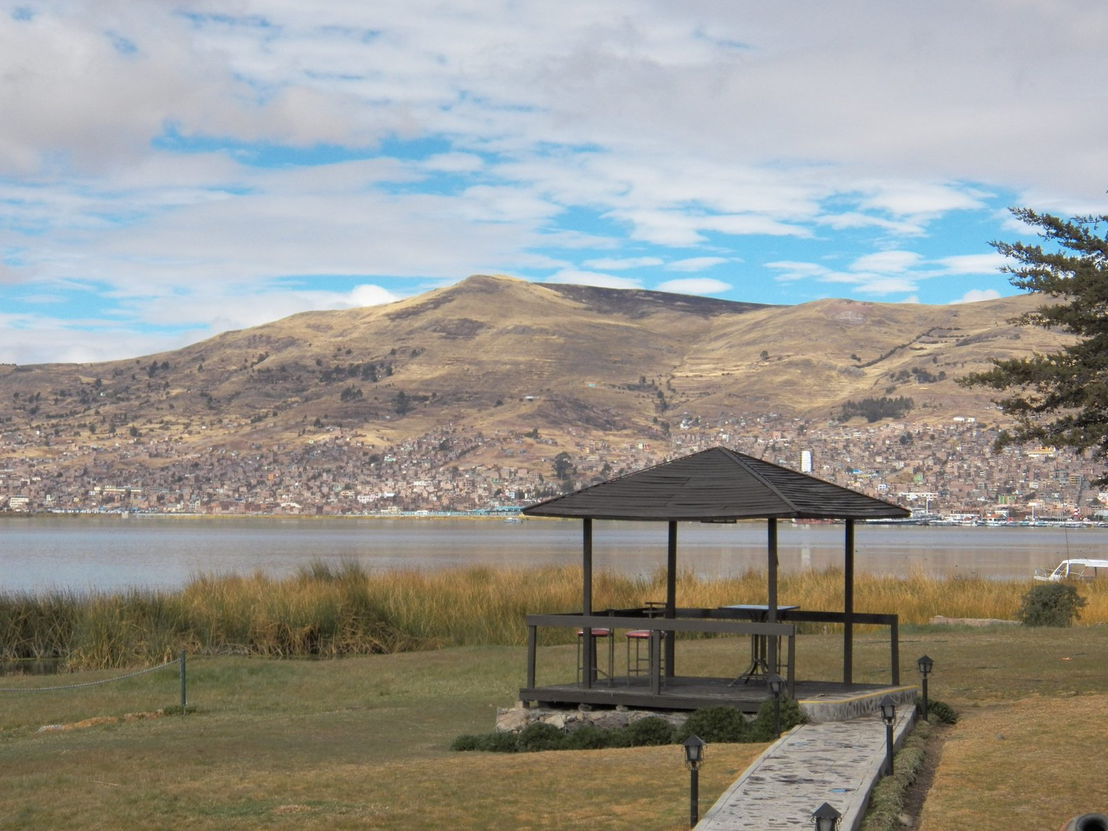 Titicaca-meer met Puno in de achtergrond en overdekt houten terrasje op voorgrond.