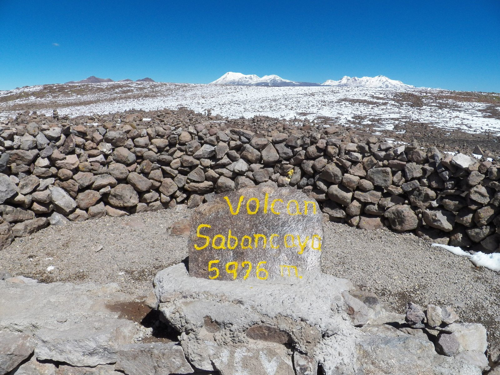Gele letters op steen: Volcan Sabancayo 5976 m in rotsachtige vlakte.
