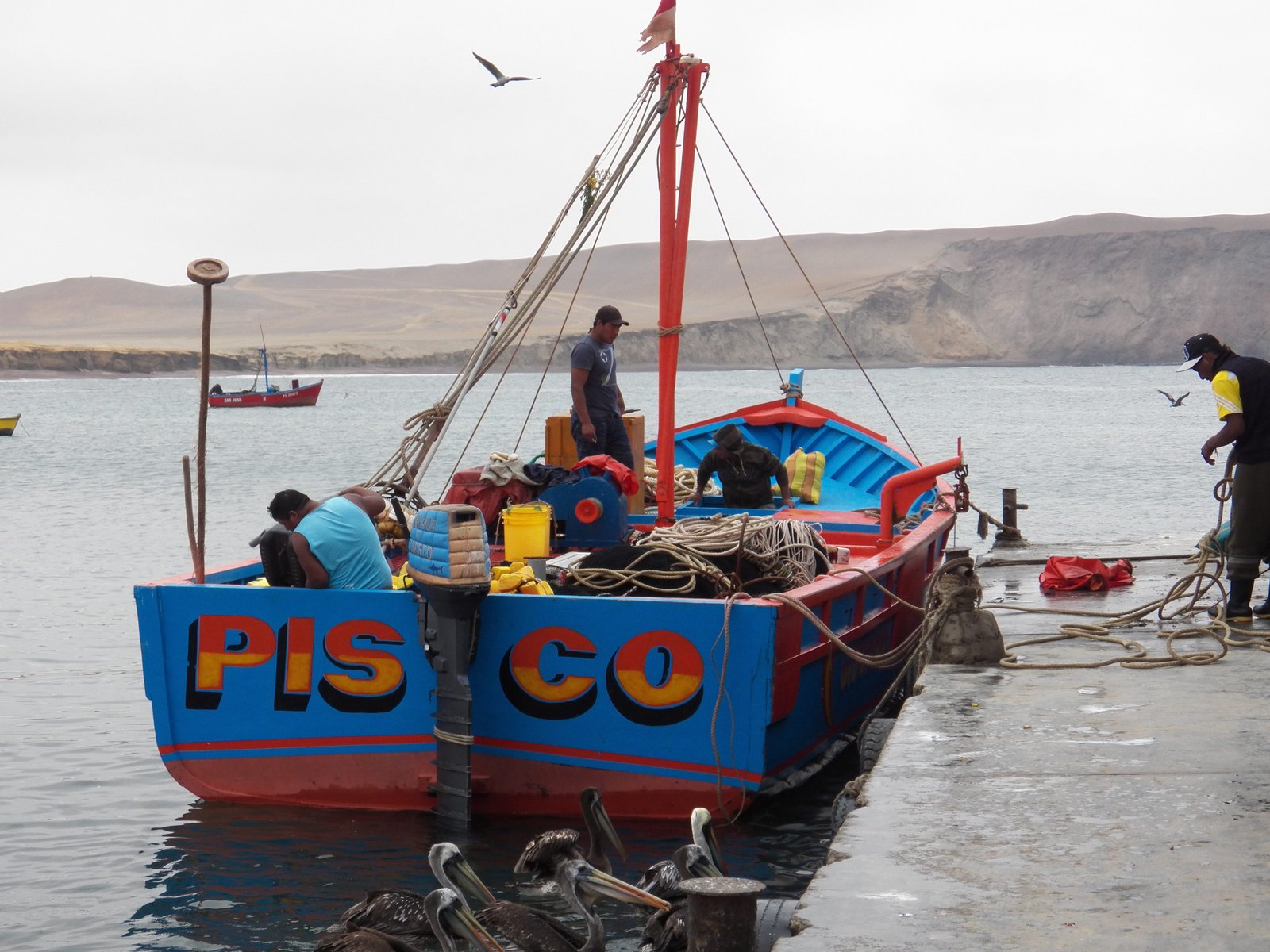 Blauwe vissersboot aan de kade met in oranje letters "Pisco".