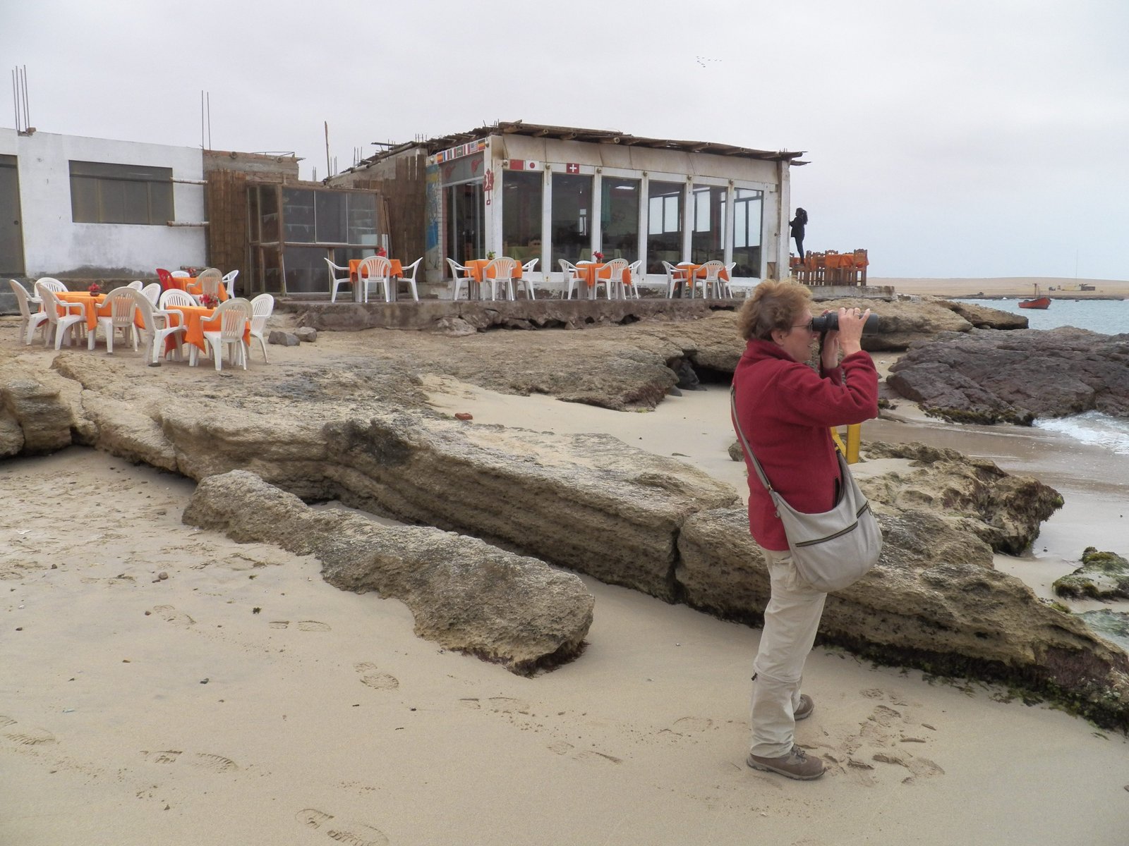 Toeriste op rots- en zandstrand voor vervallen café.