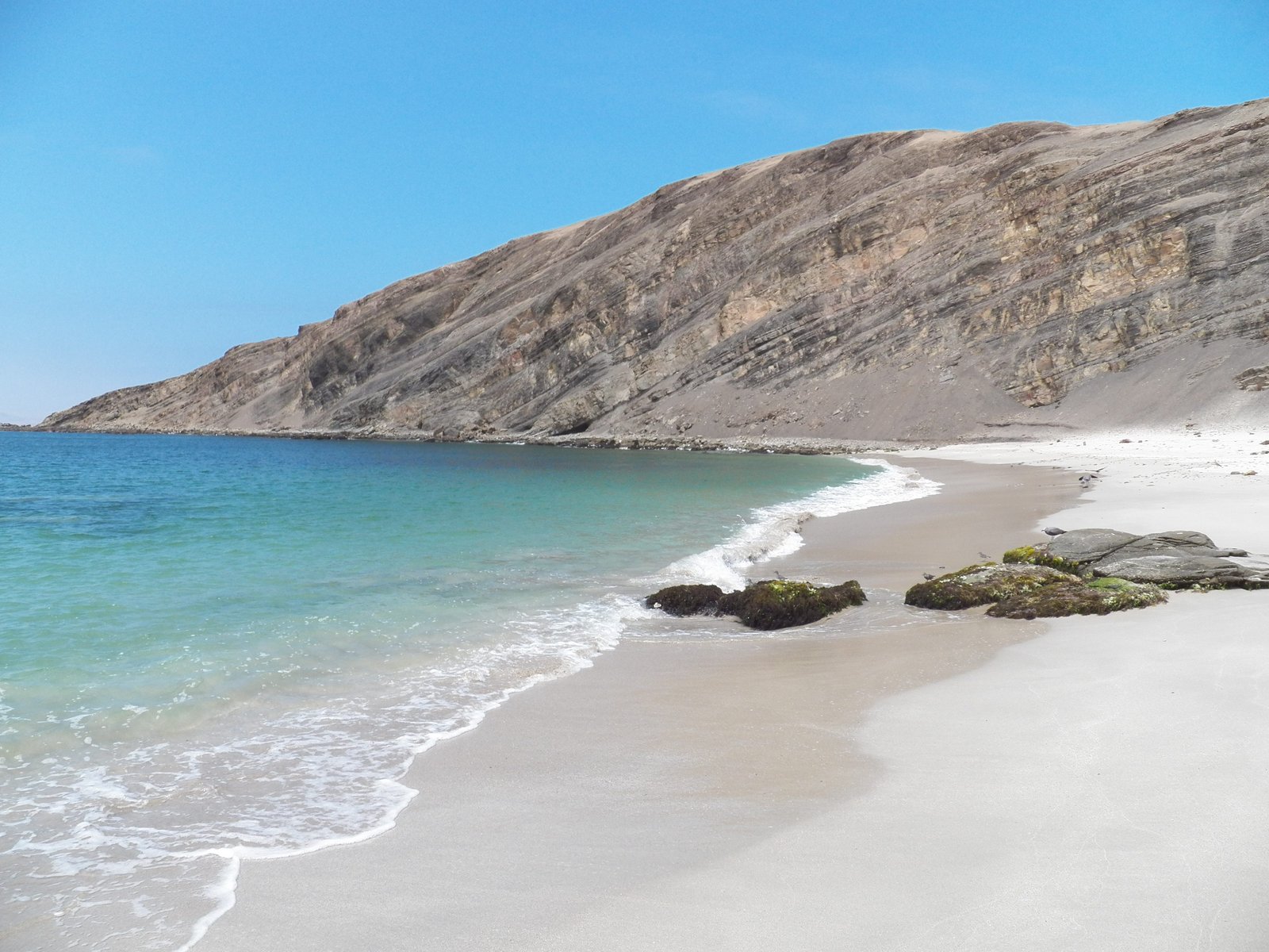 Grijs-wit strand en rotsen met azuurblauwe zee.